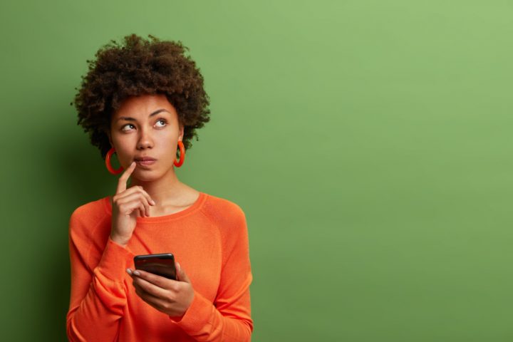Mulher com blusa laranja considerando site de pesquisa remunerada