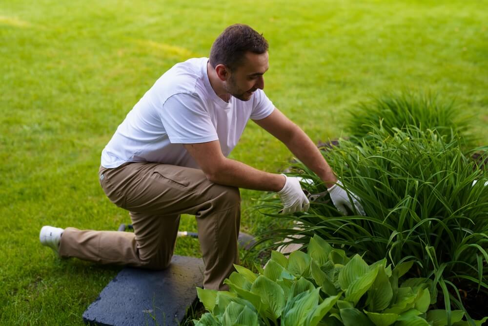 Imagem de um homem trabalhando na manutenção de um jardim como fonte de renda extra.